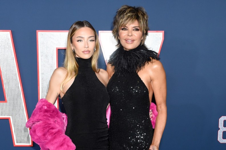 Lisa Rinna and Delilah Belle Hamlin posing in black dresses in front of a navy blue backdrop.