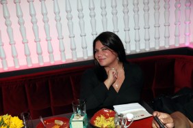 Karen Gravano sitting at a table full of food and smiling while wearing a black dress