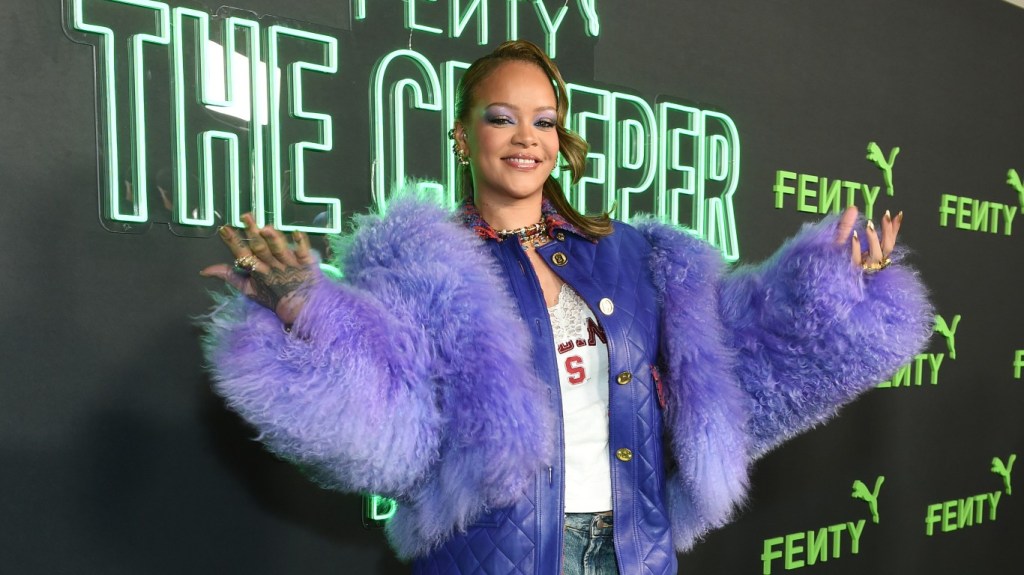 Rihanna holding her arms up and posing in a purple fur coat