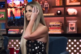 Kim Zolciak on Watch What Happens Live wearing a black dress and fixing her hair while making an awkward facial expression