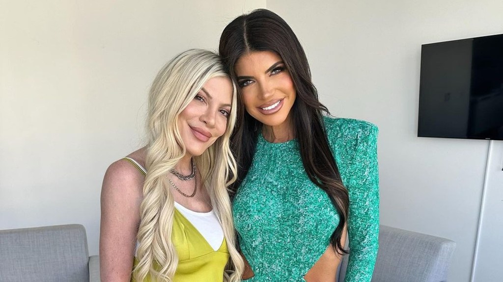 Tori Spelling in a yellow top posing with Teresa Giudice, who is wearing blue