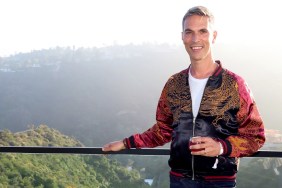 Ari Shapiro in a red and black jacket standing in front of a mountain on a balcony and holding a glass of wine