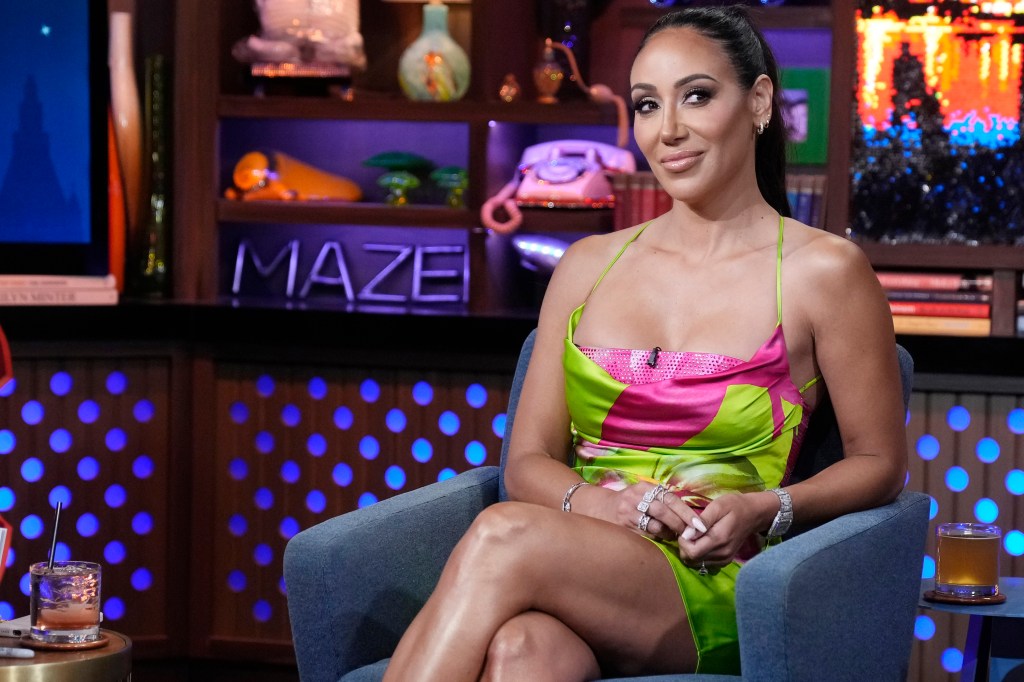 Melissa Gorga sitting with her legs crossed in a green and pink dress on Watch What Happens Live