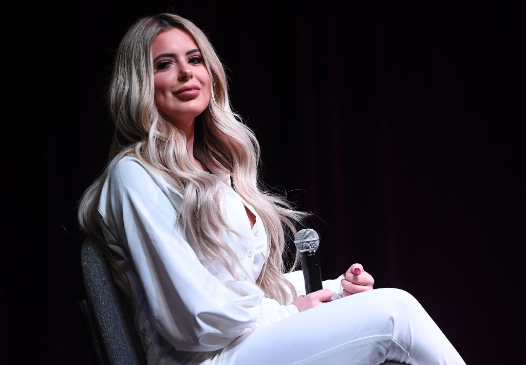 Former Bravolebrity, Brielle Biermann seated with a microphone wearing white.