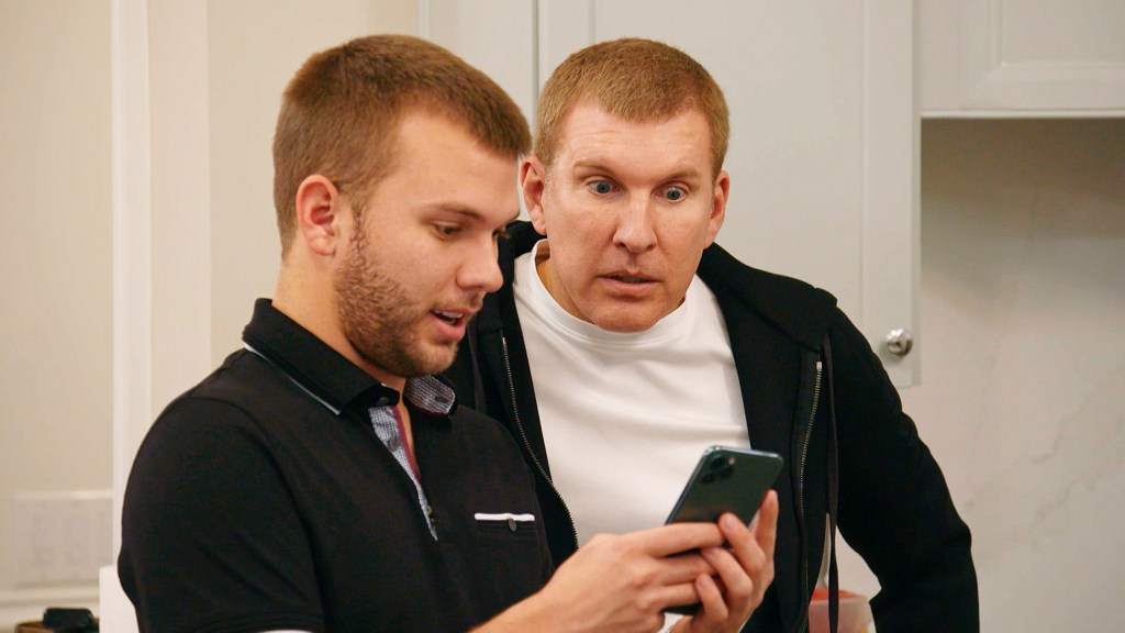In a screen grab from Chrisley Knows Best, Chase Chrisley is showing something to Todd Chrisley on his phone