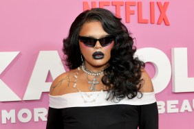 Kandy Muse in a black dress wearing black sunglsses in front of a pink backdrop