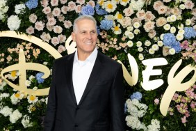 Mel Owens in a black suit posing in front of the Disney logo and a wall of flowers
